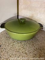 Green oval cast iron pot with lid on countertop, showing front and side view of pot and handles.