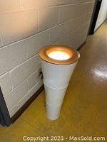 Full side view of the entire floor lamp showing white conical body and gold top ring on a yellow tile floor near a cinder block wall