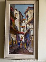 Frontal photo of the vintage oil on canvas painting depicting a street scene with buildings and two walking figures, framed with light textured frame.