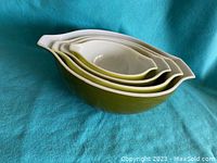 Side view of 4 vintage olive green Pyrex nesting bowls stacked inside each other, white interior and spouts visible.