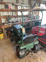 Rear view of the vintage green antique tractor highlighting the large rear tires, black seat and roof frame structure, showing condition and wear.