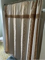 Beige decorative shower curtain with floral pattern and brown fringe trim hung on a shower rod