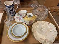 Overview of assorted china dishes including plates, teacup, mug, decorative vase, and cut glassware in a box.