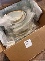 Photo of cardboard box with five wrapped porcelain serving dishes with different colored trims (gold, silver, green).