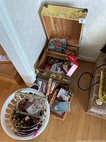 Golden decorative wooden chest opened showing assorted Christmas ornaments and boxes inside, plus additional items in a white laundry basket next to the chest.