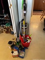 Photo of the entire lot showing vacuum, mop, red bucket with tools, and various cleaning and gardening product bottles on the floor.