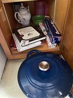 Photo showing blue ceramic pot with lid, white ceramic teapot with floral design, green bowl, assorted cookbooks (including Downton Abbey Cookbook), and boxes of Reynolds Wrap tin foil and Glad plastic wrap inside wooden cabinet.