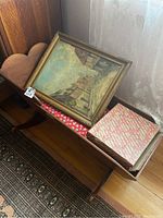 Wooden cradle holding framed painting and file box, showing the cradle's heart-shaped backrest and overall finish.