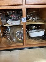 Cabinet with stacked baking dishes, metal pots, pans, lids, strainer, and grater visible