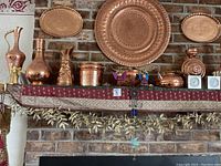 Front view of fireplace mantle showing copper decorative trays and vessels on runner with gold leaf garland beneath