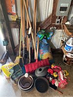 Photo of gardening tools including shovels, brooms, red shovel, flower pots, and several bags of soil amendments on floor