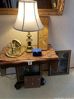 Photo of hallway table with brass lamp, brass carousel music box, blue jewelry box, and paintings.