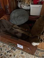 Wooden drawer open with items inside including a greenish-gray checkered flat cap hat, a brown fuzzy hat, and a brown suede purse with strap and white fur trim.