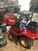 Front-side view showing red hood, 'Huskee' branding, front tires, deck and steering wheel