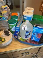 Overview of the lot showing paper plates, paper baking cups, dish detergent, disinfecting wipes, Ziploc bags, paper towels, and a Hamilton Beach blender base.