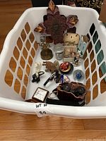 Full view of knick-knacks lot in a white laundry basket showing assortment of figurines, wall decor, binoculars, flashlights and clock.