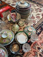 Wide view showing stacked ornate bowls with lids, metal condiment container, ceramic spoons, and clear glass bowls arranged on oriental carpet.
