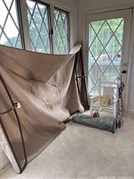 Beige fabric sunporch furniture frame leaning against wall with windows