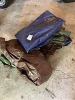 Photo showing folded tarps in various colors and sizes, including blue, brown, and green tarps stacked on top of each other.
