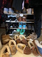 Overall view of multiple pairs of women's shoes including slippers and casual shoes arranged on a shoe rack and floor, showing a variety of styles and conditions.