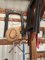 Two black folding sawhorses hanging on a wooden beam, a gardening straw hat hung on the lower left sawhorse, and metal socket bars below, inside a metal shed.