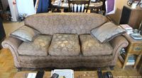 Front view of the antique Chesterfield couch showing three seat cushions and four pillows, brown floral upholstery.