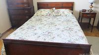 Queen size bed made with floral bedspread and matching pillow shams visible on wooden bed frame.
