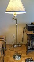 Photo of a tall brass floor lamp with a conical fabric shade, showing the full height and base, in a room setting.