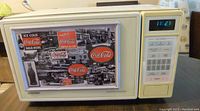 Hotpoint microwave oven with closed door showing decorative Coca-Cola metal sign attached with magnets.