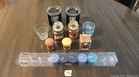 Photo shows 11 items on brown wood table: 6 small taper candles in plastic container, 2 black/silver ribbed candle holders, 2 clear ribbed votive candle holders, and 5 small scented candles in glass and cardboard packaging.
