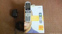 Sanyo flip phone opened and standing on original retail box with its two chargers to the side on brown surface.