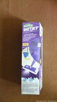 Photo showing unopened original box of Swiffer WetJet floor cleaner, purple and white packaging with product details and images.