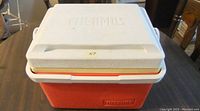 Red and white Thermos cooler with closed lid showing embossed branding and locking handle.