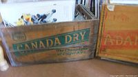 Side view of Canada Dry wooden crate featuring green lettering 'Canada Dry' and slogan 'The Champagne of Ginger Ales'.