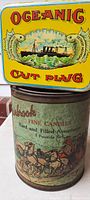 Stacked view of the two tins showing the Oceanic Cut Plug tin on top with bright yellow, red, and green graphics, and the Uabrook Fine Candies tin underneath with a horse carriage graphic.