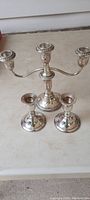 Silver 3-arm candelabra and two single candle holders arranged vertically, showing detailed front view and overall shape.