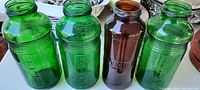 Four heavy glass antique refrigerator jars, three green and one amber, showing embossed lettering on the sides.