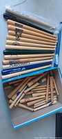 Close-up of additional small wooden baseball bats in box showing various printed sports logos and advertising.