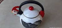 Side view showing the body, handle, lid, and rooster head pour spout of the metal tea pot.