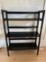 Full front view of black 3-level folding shelving unit showing overall construction and design.