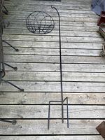 Tall black iron spiked plant holder with two metal stakes for sinking into the ground, shown fully extended on wooden deck.