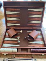 Open vintage leather backgammon case showing board with cream and cinnamon triangles, playing pieces in two compartments, two dice cups, dice and doubling cube placed on the board.