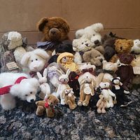 Full view of all 26 plush animals arranged together on black textured surface against plain background. Shows variety of teddy bears, bunnies, rabbits, dogs, cats, and moose in different colors and materials.