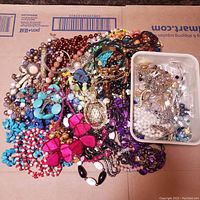 Wide view of assorted costume jewelry including colorful beaded necklaces, pendants, and bracelets spread out on cardboard.