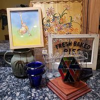 Frontal wide view of all items in the lot including monkey artwork, stitchery, vases, pitcher, stained glass kaleidoscope, milk bottles, and framed sign on a granite countertop.