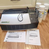 Oreck XL Professional Air Purifier with power cord, two cans of cell cleaner spray, and owner's manual placed on floor.
