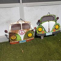 Two metal wall art pieces of VW vehicles on grass in front of a white wall.