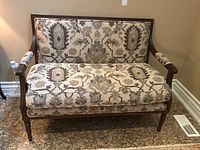 Front facing photo of bench highlighting wood frame, padded floral patterned upholstery on backrest, arms, and loose seat cushion with the cushion aligned.