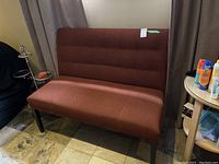 Front view of brown tufted upholstered bench with wood legs on tiled flooring near curtains and side tables.