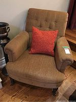 Front view of the brown upholstered armchair showing the button-tufted backrest and orange decorative cushion on seat.